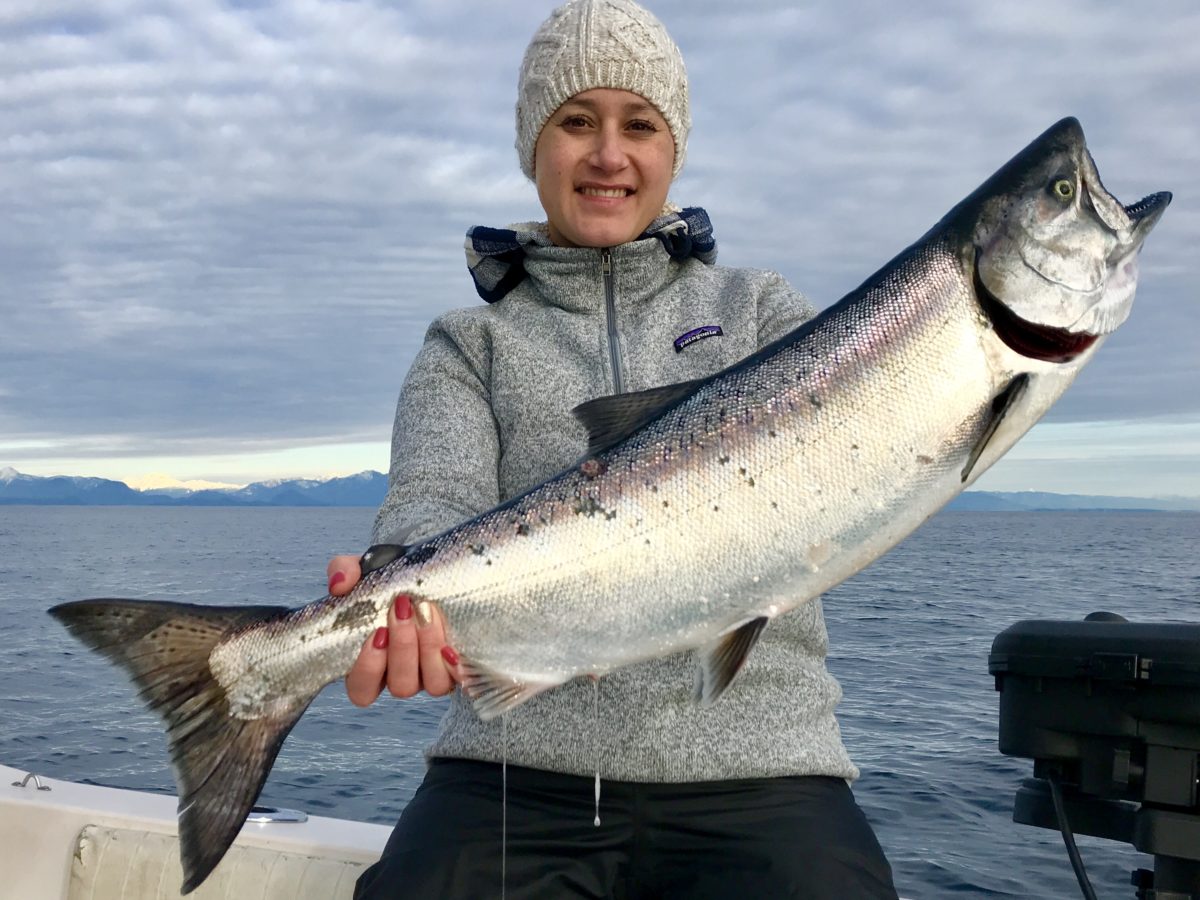 A woman in a grey hoodie and toque holding a large salmon
